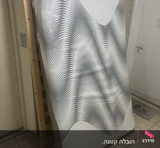 מזרן עטוף בניילון מונח על מסגרת עץ